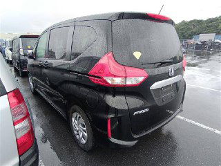 Вид сзади и сбоку чёрного Honda Freed 2021 на стоянке ярда, видны задние фонари, багажник и боковая часть автомобиля, мокрый асфальт вокруг.