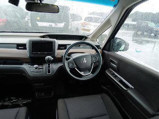 Салон Honda Freed 2021: вид на руль, мультимедийный экран, передние сиденья и обзор лобового стекла на парковку ярда, аккуратное состояние интерьера.