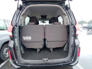 Открытый багажник Honda Freed 2021 с откинутыми задними сиденьями, видна вместительность грузового отсека и мокрый пол стоянки на ярде в Японии.