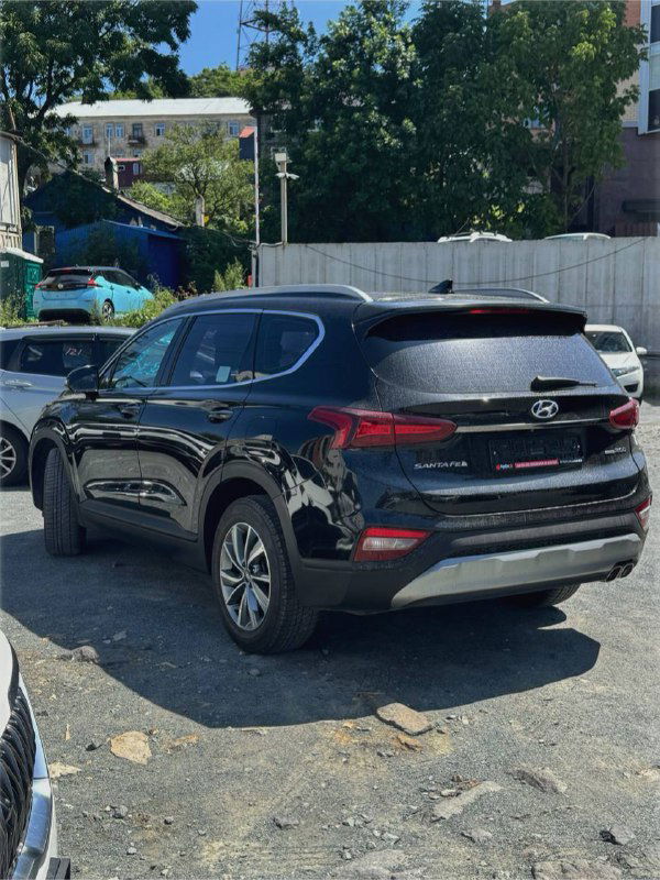 Hyundai Santa Fe 2019, вид сзади и в профиль: задняя часть кроссовера, распоряжение багажника и задние фонари на фоне автостоянки.