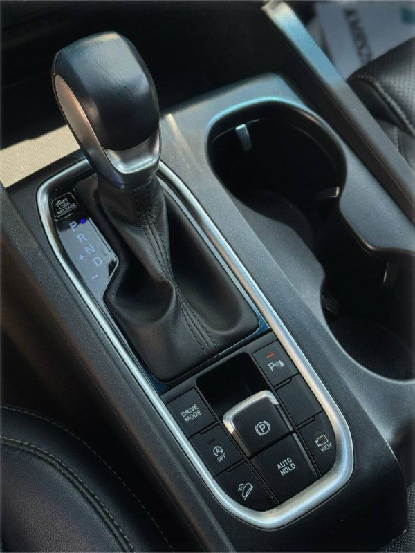 Селектор коробки передач Hyundai Santa Fe 2019 и окружение подстаканников: крупный план центральной консоли и кнопок рядом с рычагом.