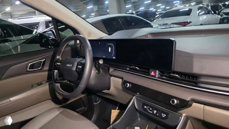 Вид на переднюю панель и центральную консоль KIA Carnival 2024: большой мультимедийный экран, панели управления климатом и элементы отделки салона.