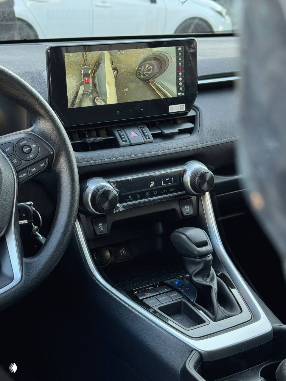 Интерьер: центральная панель с крупным сенсорным дисплеем и видом камеры 360°, органы управления климатом и селектор коробки передач видны крупным планом.