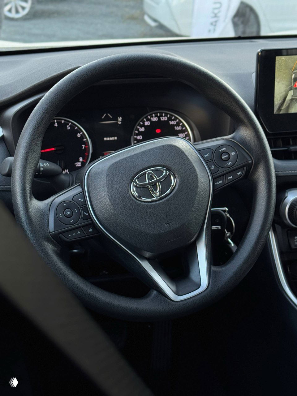 Вид на руль Toyota RAV4 с логотипом Toyota, комбинация приборов и органы управления на руле, крупный план рулевой колонки и индикаторов.