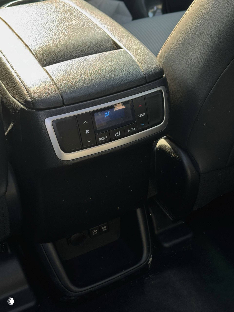 Панель управления климатом и подлокотник между сиденьями с дисплеем для задних пассажиров в Toyota Highlander, крупный кадр центральной консоли с розетками.