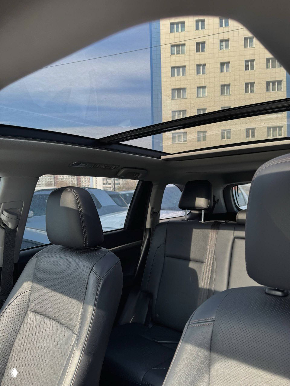 Панорамная крыша и передние кресла Toyota Highlander, светлый вид через люк, интерьер в дневном освещении, видно потолочную консоль и опоры.