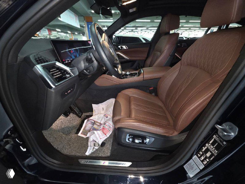 Салон BMW X6 2024 с коричневыми кожаными передними сиденьями, руль, панель приборов и центральная консоль, вид со стороны водителя.