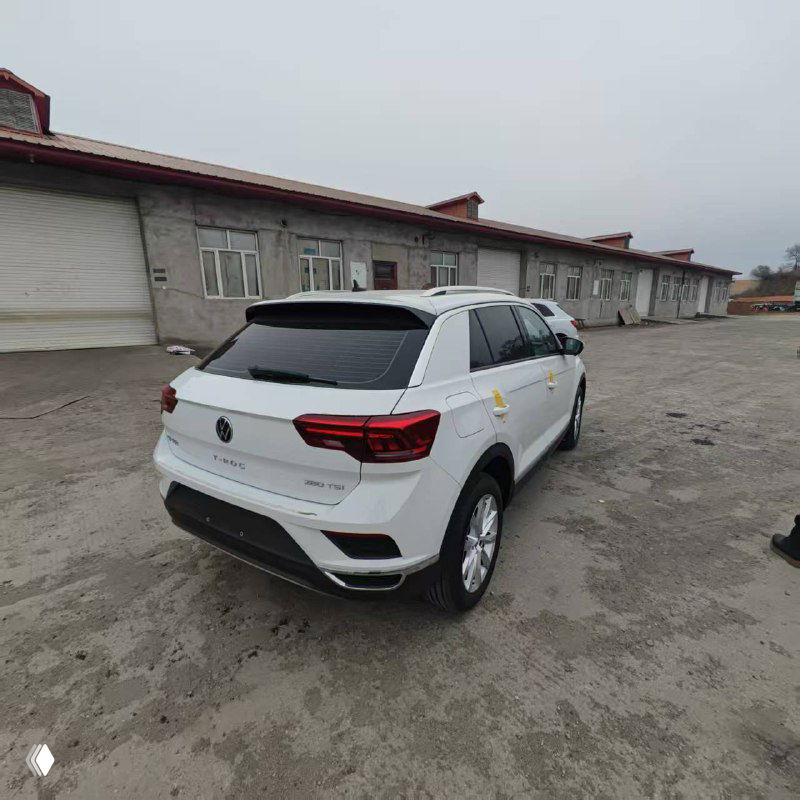 Volkswagen T‑ROC, вид сзади: белый кроссовер у склада, крупный план задней части и багажника, подготовлен к отправке, вокруг промышленные постройки.