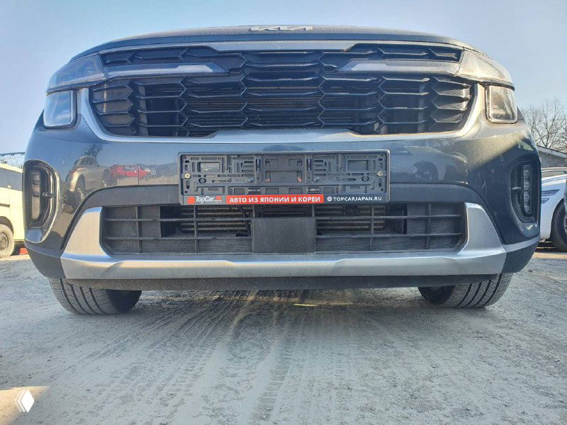 Крупный план передней части KIA Seltos 2022: решётка радиатора, нижняя часть бампера и крепление номерного знака на стоянке импорта.