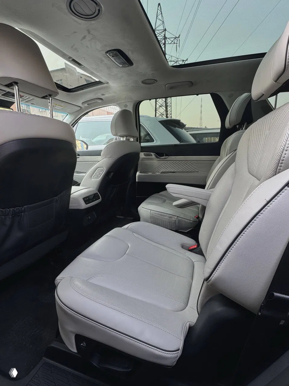 Задние сиденья Hyundai Palisade: два ряда кресел, подлокотник и пространство для пассажиров, видна чистая светлая обивка.