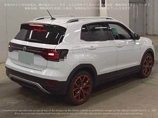Вид сзади белого Volkswagen T‑Cross 2021 на японском аукционе, задние фонари и багажник в кадре; автомобиль стоит в ангаре, номер и таблички замазаны.