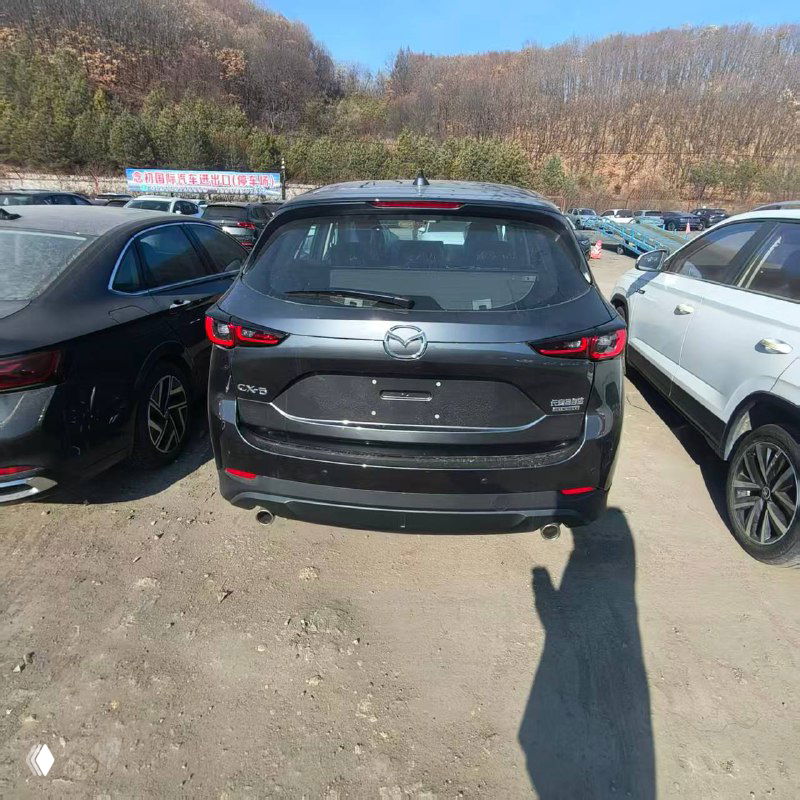 Вид сзади на Mazda CX-5 на стоянке: багажник и задние фары, автомобиль в сером цвете среди других новых машин на площадке.