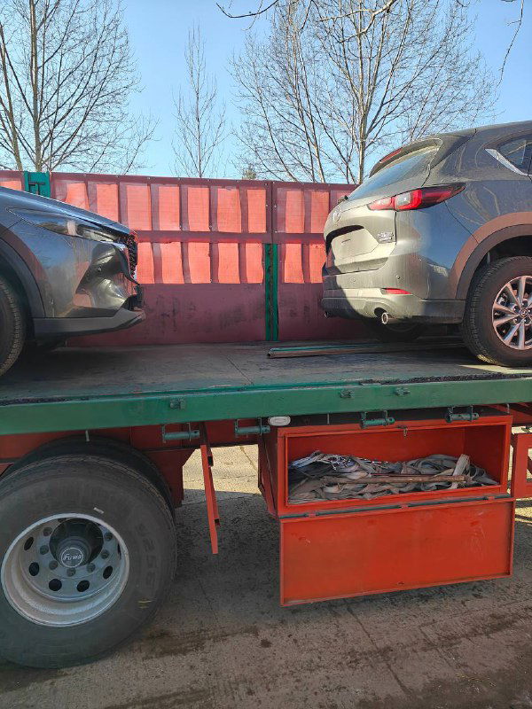 Две Mazda CX-5 на прицепе или платформе грузовика: боковой ракурс платформы с автомобилями, процесс перевозки между площадками.