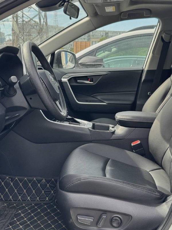 Передние сиденья салона Toyota RAV4 в комбинации ткани и кожи, вид со стороны пассажирской двери, показаны подлокотник и пространство кабины.