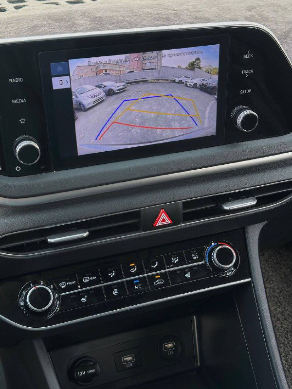 Мультимедийный экран с изображением камеры заднего вида и часть центральной консоли с климат-контролем и кнопками управления.