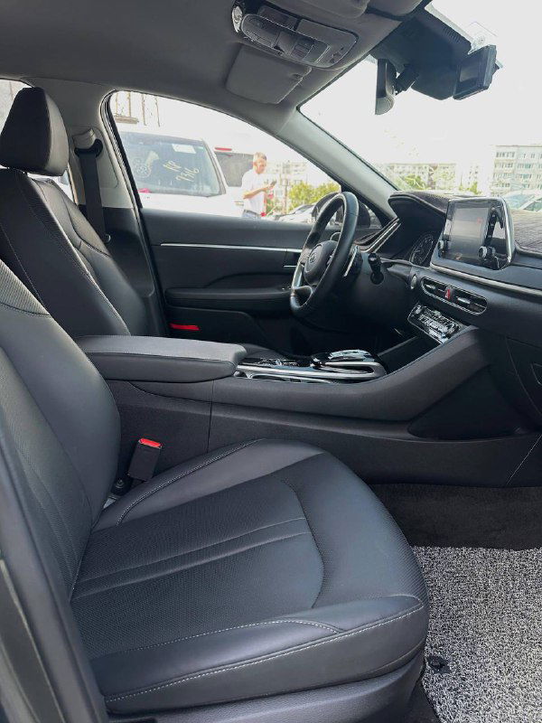 Вид на передние сиденья и салон справа: чёрная обивка, центральный подлокотник, панорамный обзор салона и элементы дверной обшивки.