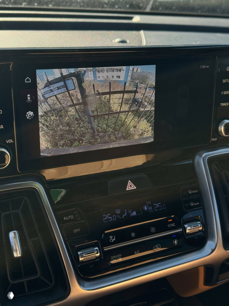 Экран мультимедиа показывает изображение с камеры заднего вида, внизу видны органы управления климатом и подсветка цифрового дисплея, интерьер в теплых тонах.