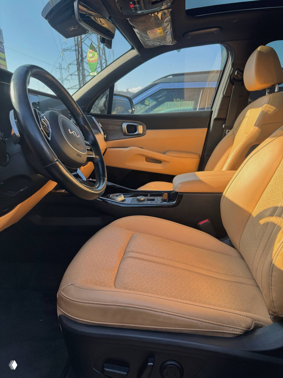 Вид на переднее пассажирское место и водительскую зону: бежевые кресла, панорамная крыша, рычаги регулировок кресел и контуры дверной отделки на фоне солнца.