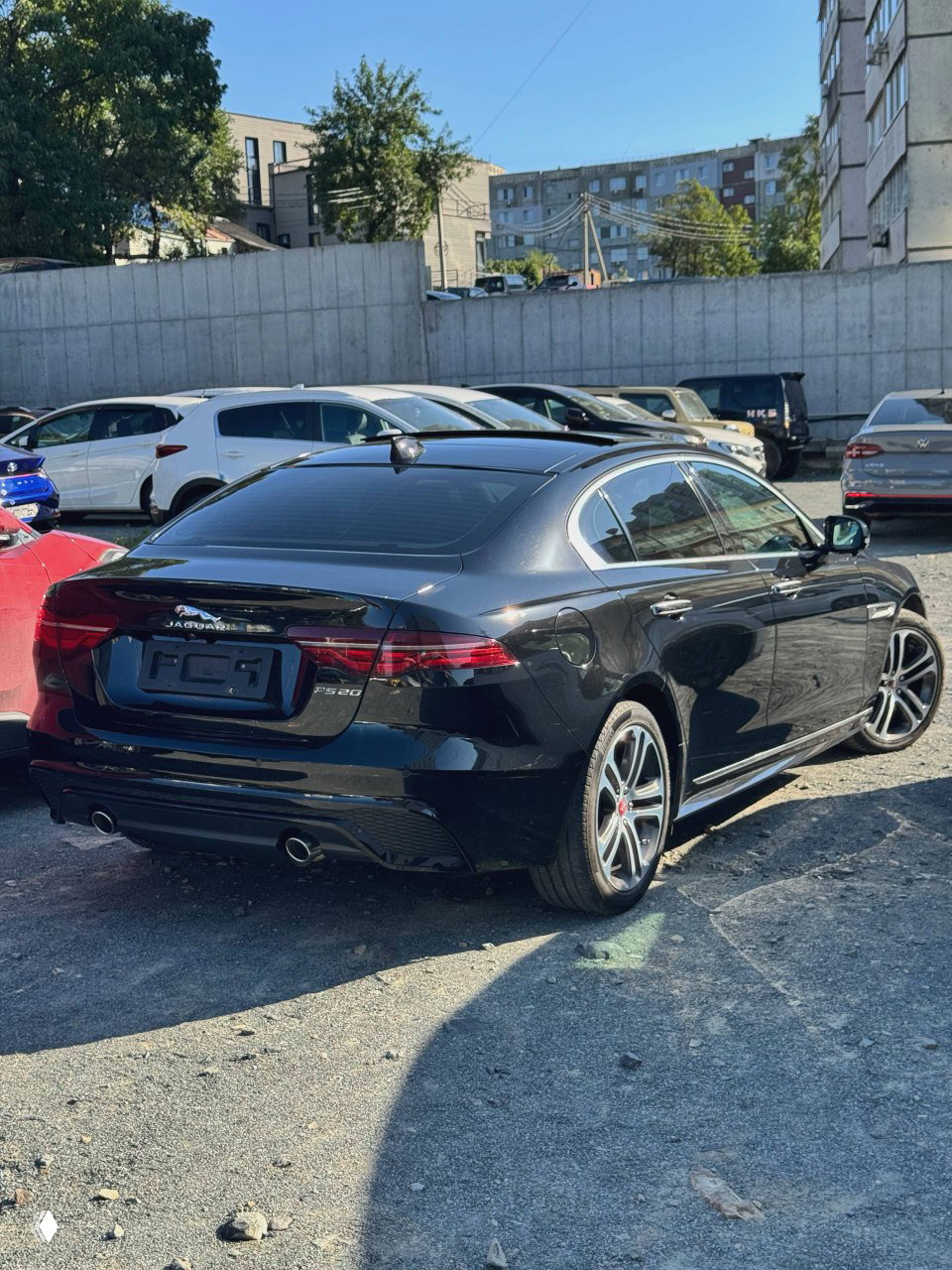 Задняя часть чёрного Jaguar XE L 2021: кузов, задние фонари, выхлопные трубы и место для госномера — автомобиль на открытой стоянке.