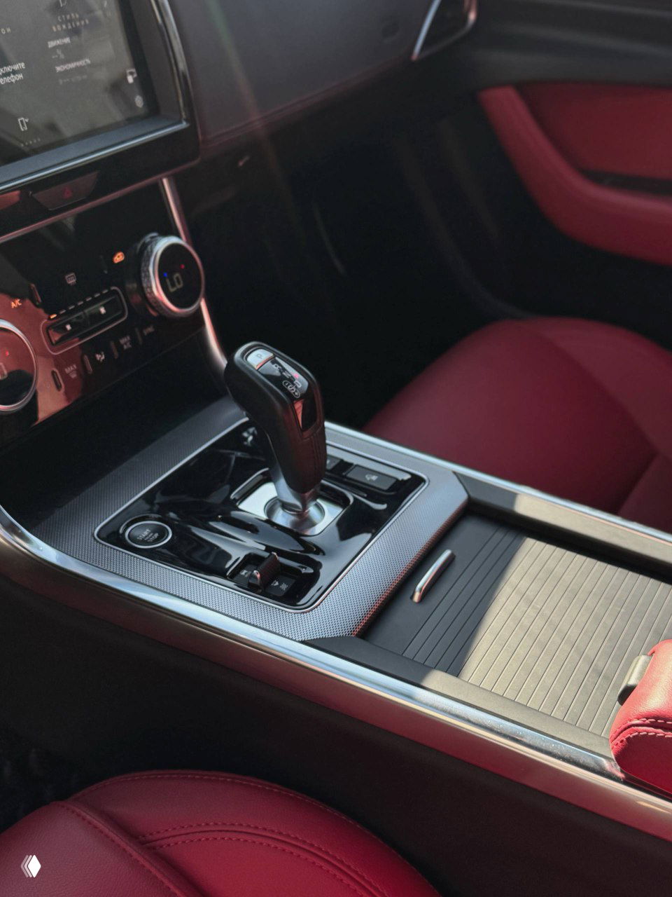 Ближний план селектора коробки передач и центрального подлокотника Jaguar XE L — видны кнопки управления и отделка вокруг рычага АКПП.