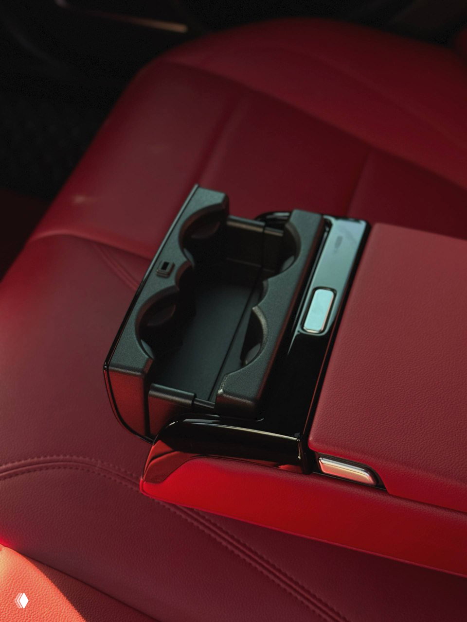 Внутренний подлокотник с выдвижным держателем для стаканов в Jaguar XE L — крупный план пластиковой вставки и швов кожаной обивки.