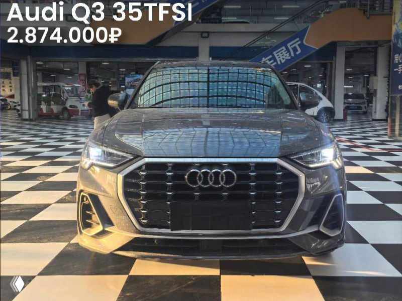 Фронтальный вид серебристого Audi Q3 35TFSI на витрине с отражением потолка и указанием цены 2.874.000₽, автомобиль без окрасов