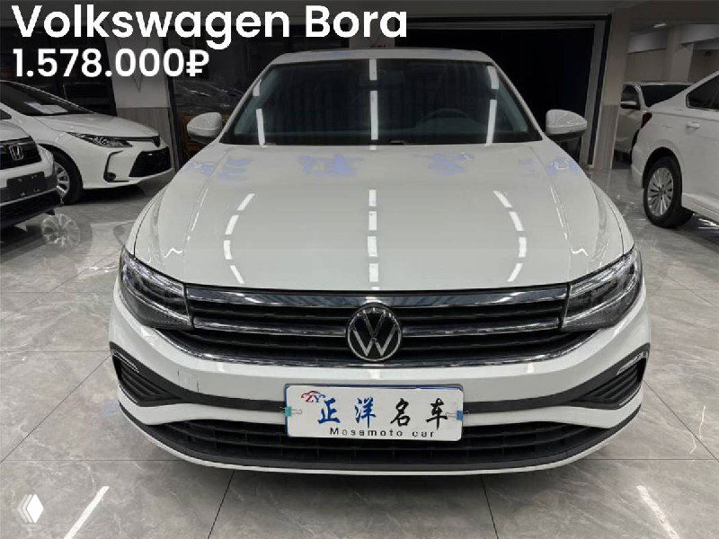 Передняя часть белого Volkswagen Bora 2023 года в автосалоне, видна табличка дилера и цена 1.578.000₽, автомобиль без окрасов