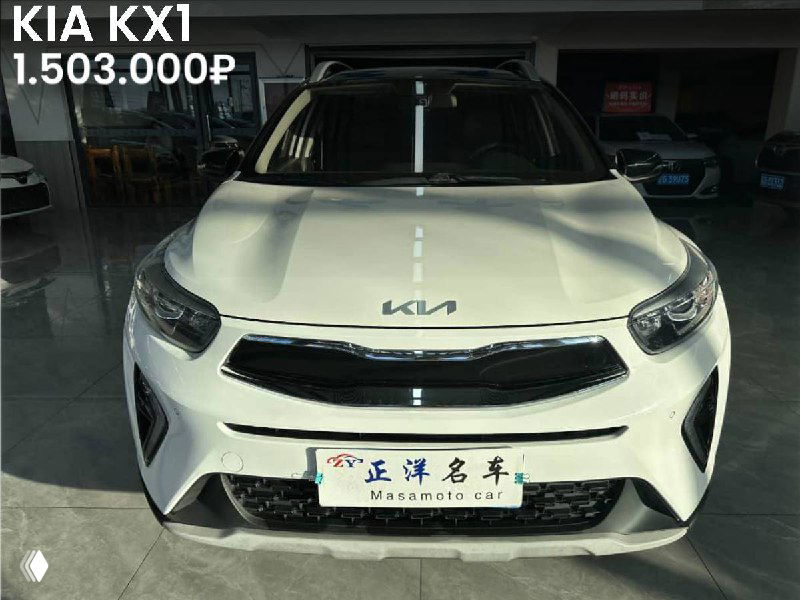 KIA KX1 светлого цвета, фронтальный ракурс в выставочном зале; на фото видно логотип KIA на капоте и цену 1.503.000₽, подчёркнута комплектация Elite.