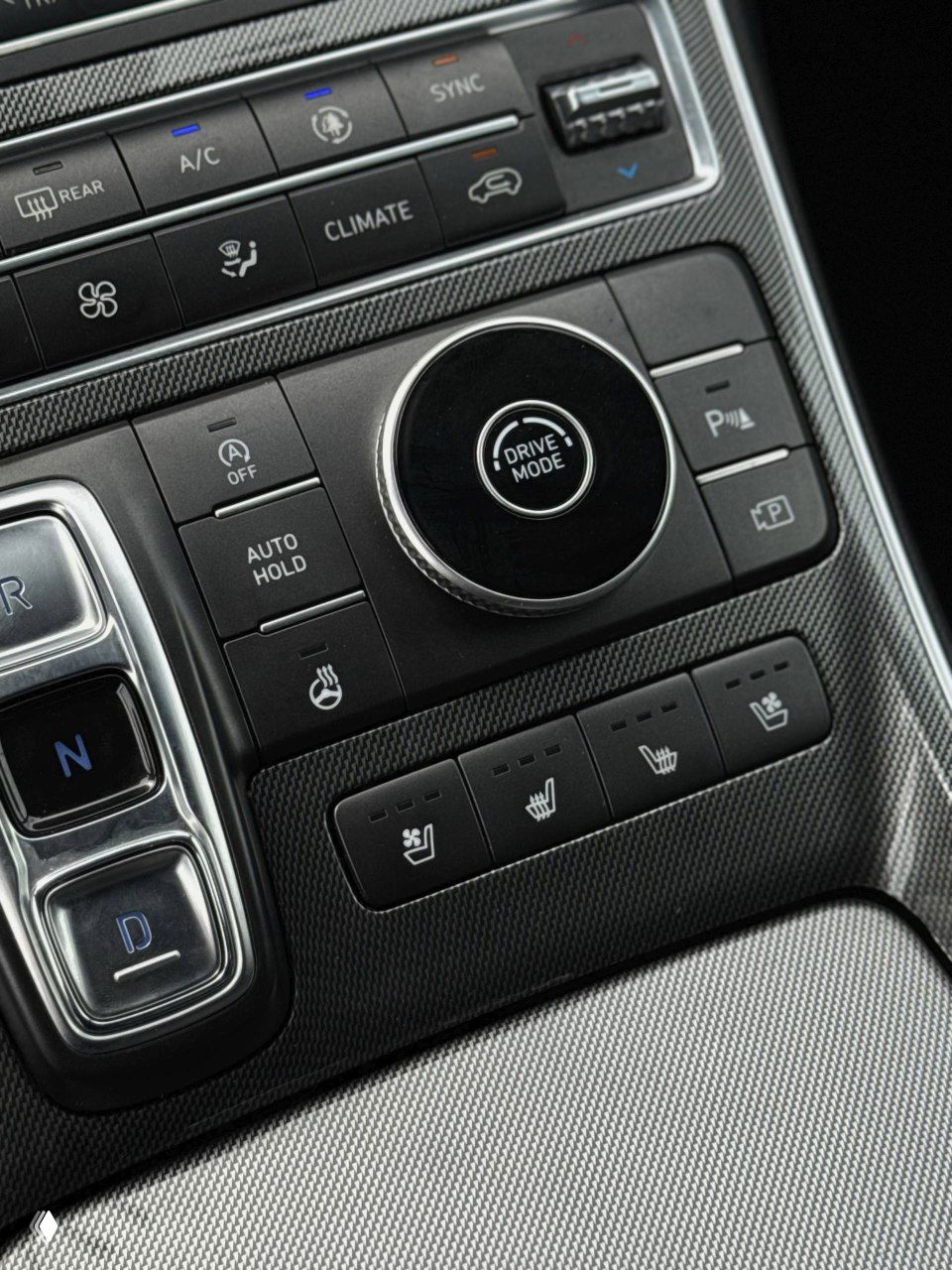 Крупный план центральной консоли: селектор режима привода, шайба Drive Mode, кнопки климата и обогрева сидений, отделка под карбон-подобную текстуру.