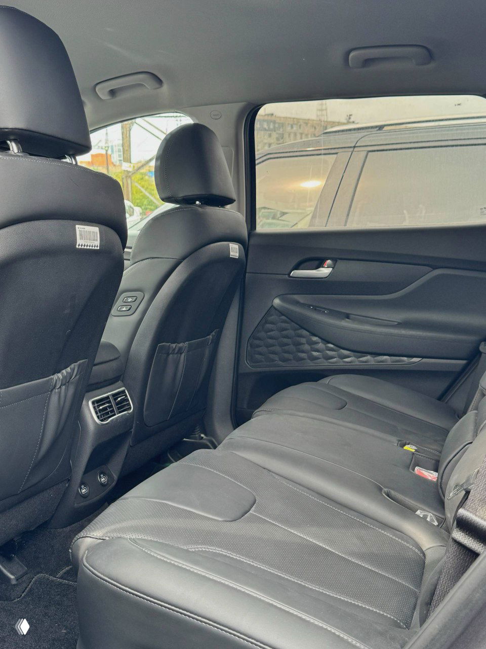Задние пассажирские сиденья Hyundai Santa Fe, обзор пространства для ног и обшивки, салон на фоне припаркованных автомобилей за окном.