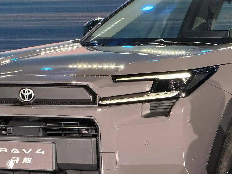 Крупный план передней части Toyota RAV4: С-образные фары, решётка радиатора и элементы переднего бампера крупным планом на презентации.