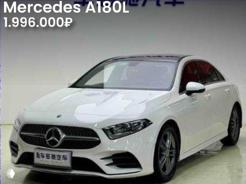 Трёхчетвертной вид белого Mercedes A180L в помещении дилера, видна передняя часть и цена 1.996.000₽; указано наличие двух окрасов в истории.