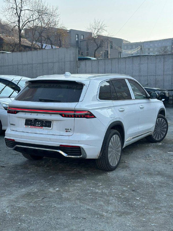 Задний ракурс белого Geely Monjaro 2025 года на стоянке; видна светодиодная сплошная стоп‑полоса, бампер и задняя часть кузова автомобиля.