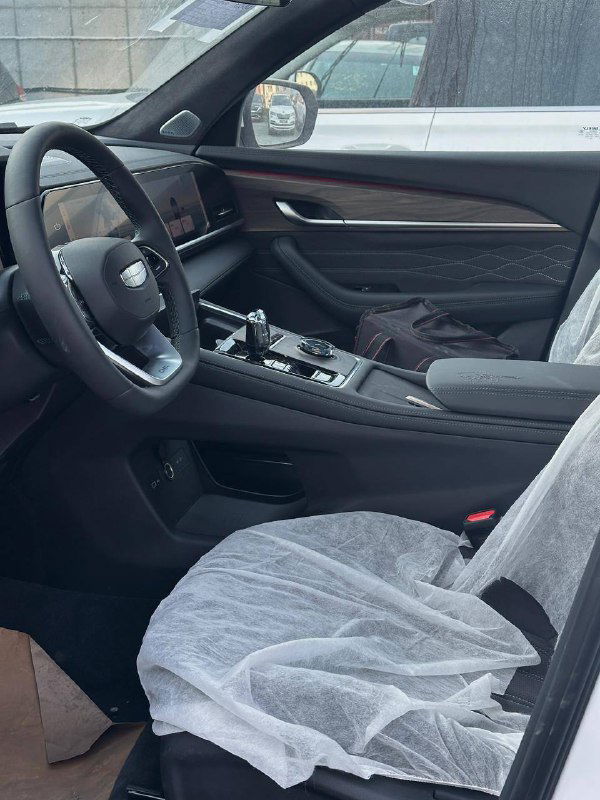 Переднее пассажирское место и центральная часть салона Geely Monjaro 2025: общий вид отделки, сиденья в защитных чехлах и консоль.
