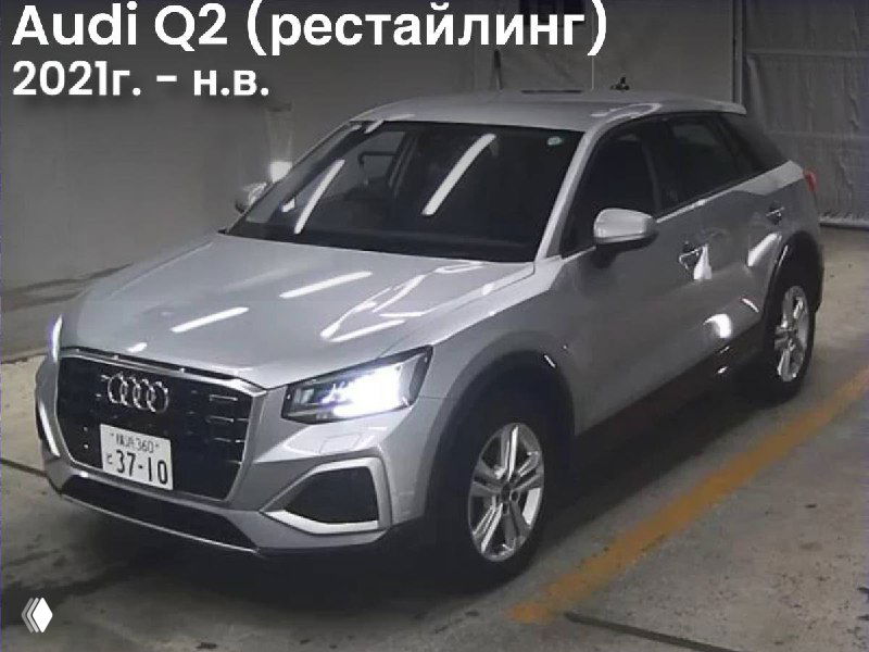 Фото Audi Q2 (рестайлинг, 2021–н.в.) серебристый кроссовер в ангаре аукциона, вид под углом; фон склада и освещение аукционной площадки.