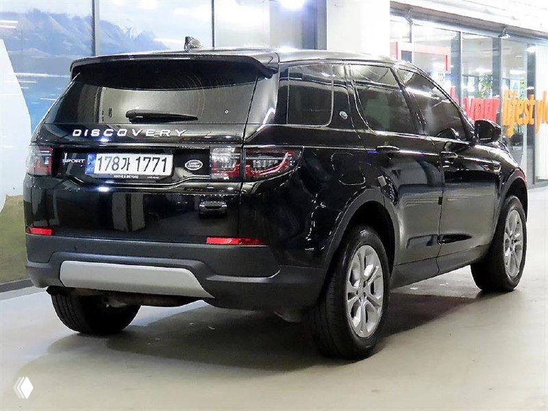 Чёрный Land Rover Discovery Sport 2020, задний ракурс в салоне автоцентра — видны фонари, задняя часть и бампер автомобиля на стоянке.