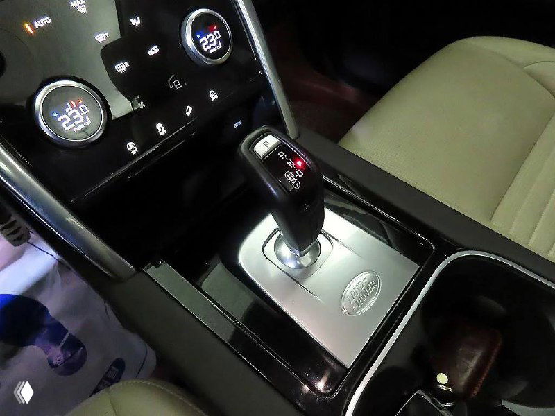 Ближний кадр селектора АКПП Land Rover Discovery Sport 2020, детали отделки, подстаканники и окантовка вокруг рычага переключения передач.