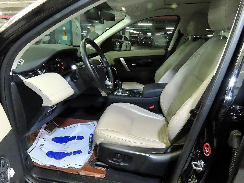 Кресло водителя и передняя пассажирская секция Land Rover Discovery Sport: кожаные бежевые сиденья, боковые панели и рулевая колонка.