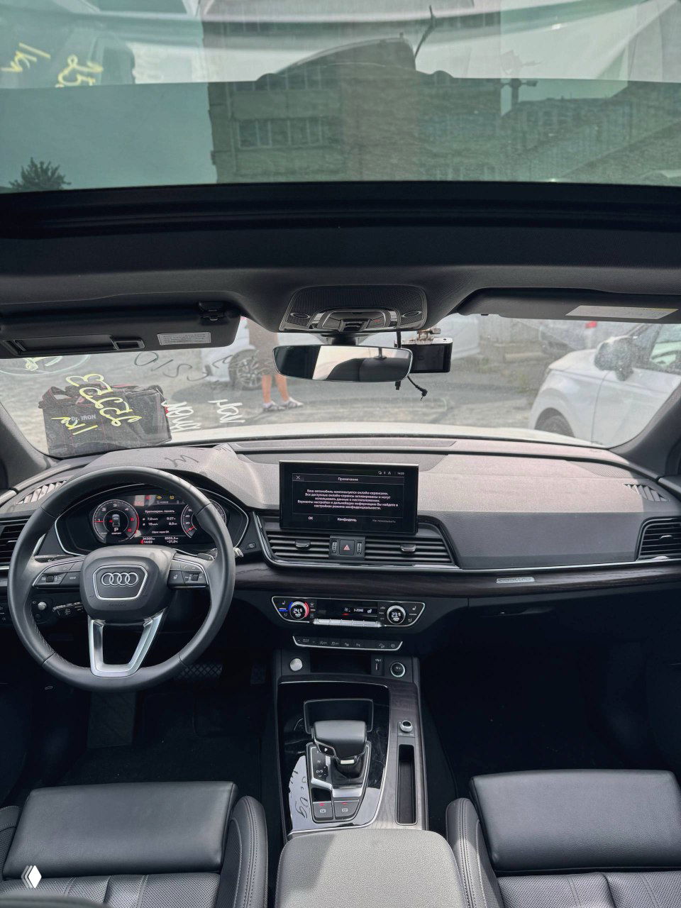 Панорамный вид салона Audi Q5 40TDI — приборная панель, центральный экран мультимедиа и передние сиденья, фото сделано через лобовое стекло.