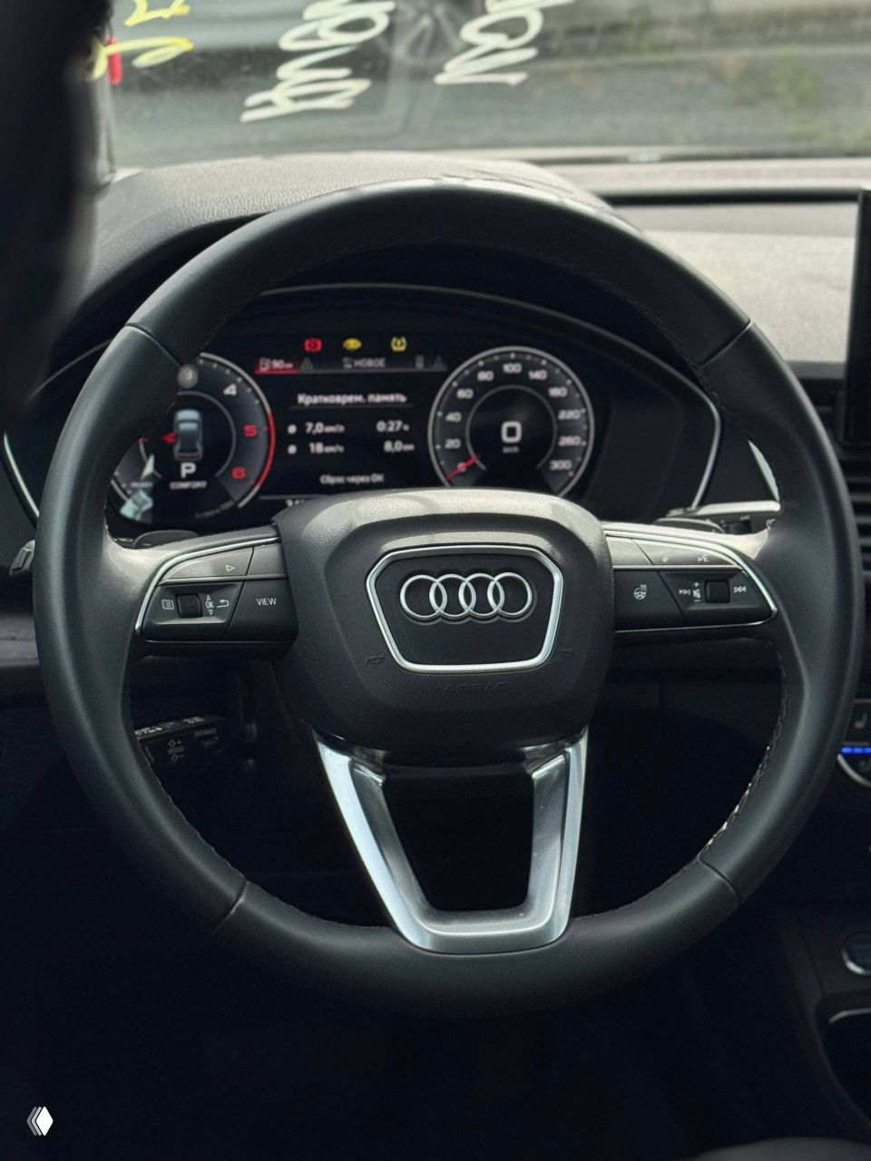 Крупный план рулевого колеса Audi Q5 с логотипом, видны кнопки мультируля и цифровая приборная панель на заднем плане.