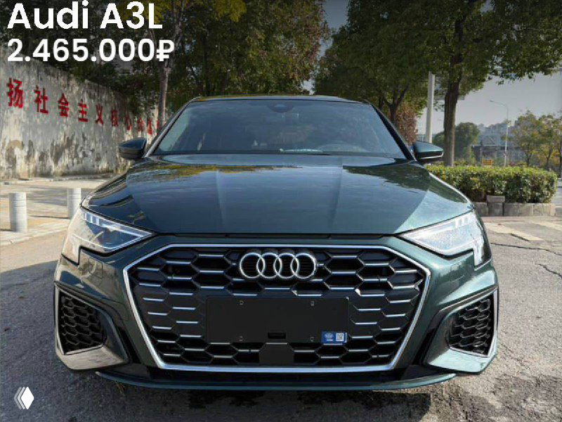 Фронтальная фотография Audi A3L 2022 в тёмном цвете на китайской площадке; видны передняя часть, решётка и цена 2.465.000₽, окружение с зелёными насаждениями.
