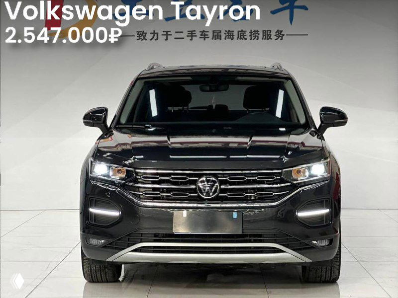 Фронтальный вид Volkswagen Tayron 2022 в тёмном цвете на выставке; чётко различимы фары и решётка, цена на изображении 2.547.000₽, нейтральный фон салона.