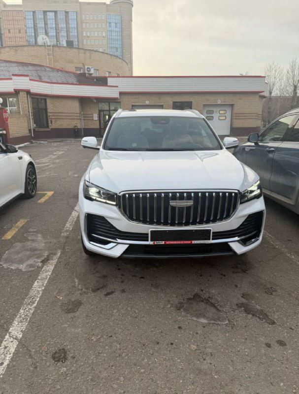 Фронтальный вид Geely Monjaro 2025 на стоянке у здания: общая композиция автомобиля после привоза, демонстрация целостного внешнего вида.