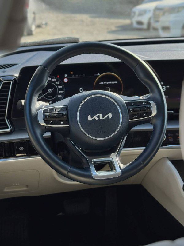 Крупный план руля KIA Sportage и части приборной панели — логотип на руле, кнопки управления и отделка салона бежевого цвета.
