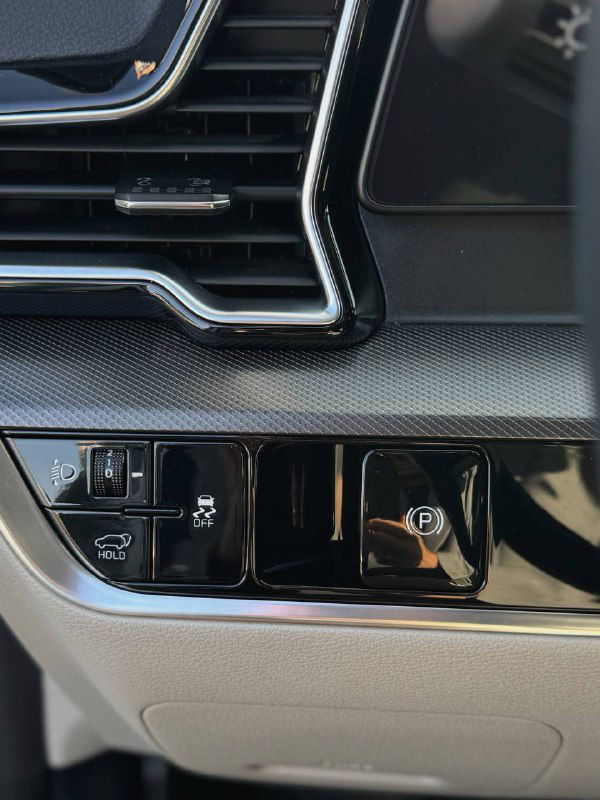 Низ приборной панели KIA Sportage с панелью кнопок — стояночный тормоз, функции безопасности и вентиляционные решётки вблизи.