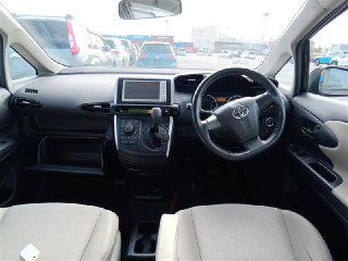 Салон Toyota Wish 2011: панель приборов, руль и передние сиденья, видно навигационный экран и чистую светлую тканевую обивку.