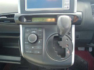 Крупный план центральной консоли Toyota Wish с селектором переключения передач, блоком климат-контроля и элементами мультимедиа на фоне коврика.