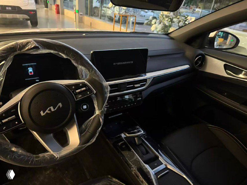 Интерьер KIA K3 — панель приборов, мультимедийный экран и рулевое колесо с логотипом, новый салон с частью защитной плёнки.
