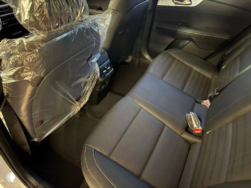 Задний ряд сидений KIA K3 с чёрной обивкой, вид на пространство для пассажиров, упаковка и ключи видимы на сиденье — новый салон.