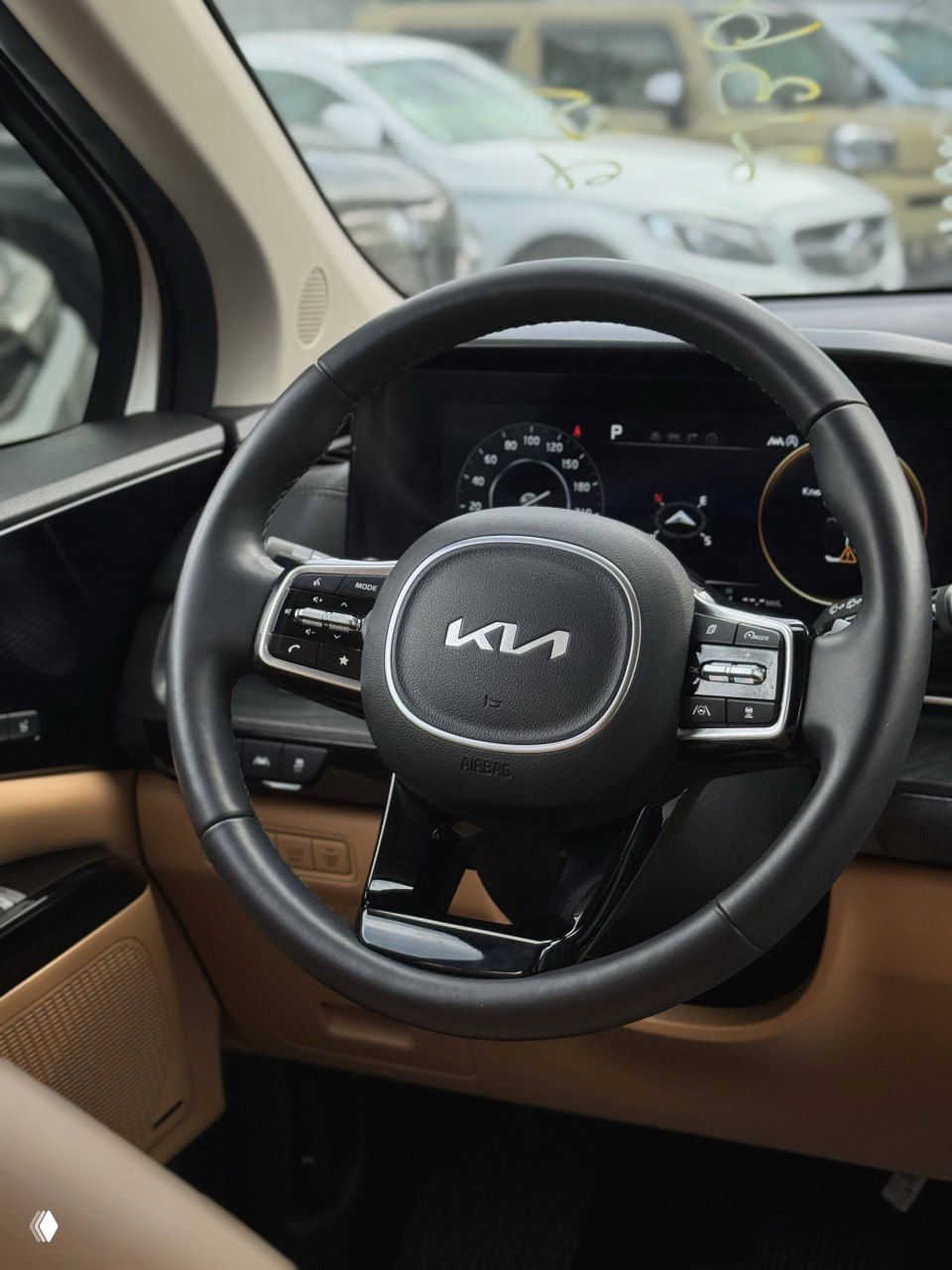 Рулевое колесо с логотипом KIA и мультирулевыми кнопками, на заднем плане цифровая приборная панель автомобиля.